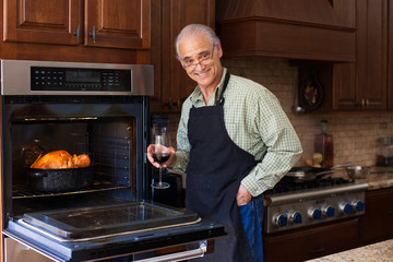Good looking senior man cooking turkey while enjoying a glass of wine