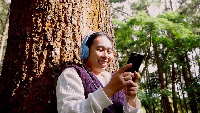 Asian young woman listening to music by headphone in the garden. Technology and relaxation concept.