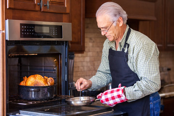 Good looking senior man basting a baking turkey