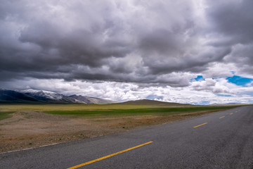 Travel forward concept background - road on plains in Himalayas with mountains and dramatic clouds.