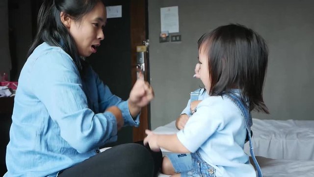 Mother and her daughter playing together in the bedroom. The child having fun to play rock-paper-scissors on the bed. Family relaxation time in vacation day.