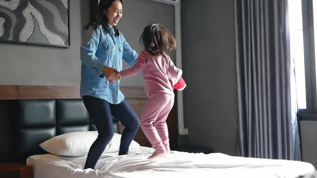 Cute little child girl laughing dancing with her mother on bed. Happy family in vacation day.