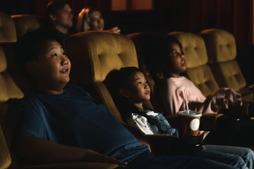 diversity children and people, american black, caucasian and asian, having fun watching movie in cinema theater