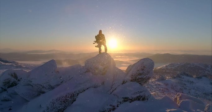 Aerial view. Freerider stands on top of the mountain, snowboard in hand. movable camera plans. Fresh powder. Extreme freeride skiers skiing from the top. beautiful storm of snow flying in the frame