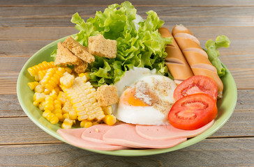 Morning menu: vegetable salad with eggs, corn, ham, hot dog placed on a wooden table