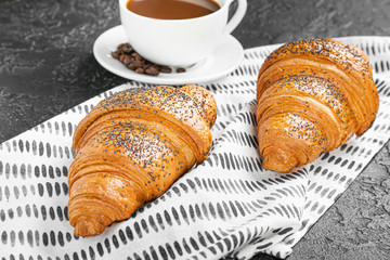 Tasty croissants with cup of coffee on dark background