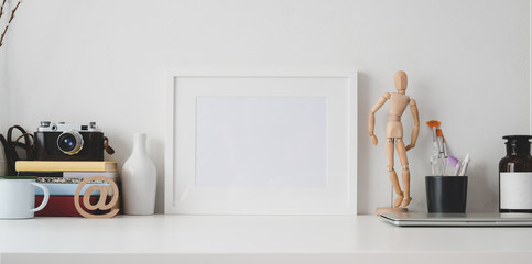 Minimal workspace with mock up frame and office supplies on white wooden table and white wall
