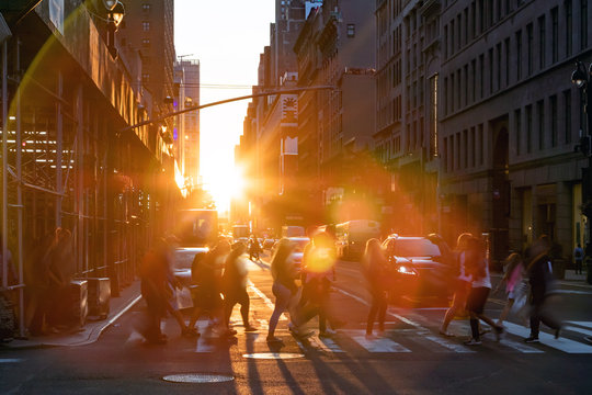 New York City - Crowds of people walking across the busy intersection on 34th Street with the bright light of summer sunset shining between the buildings of Midtown Manhattan