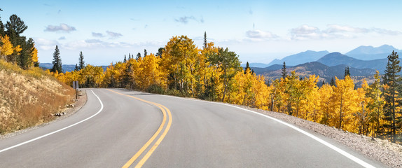 Empty road winds through a panoramic mountain landscape scene with golden fall aspen trees in the...