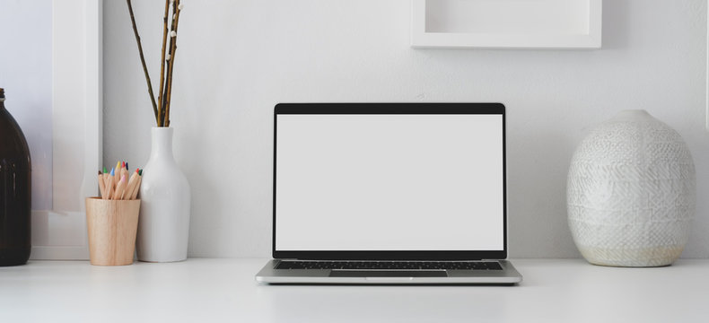Open blank screen laptop computer in minimal workplace with office supplies and ceramic vase