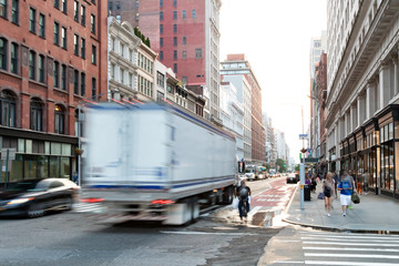 Busy view of 23rd Street with delivery truck speeding past the people walk down the sidewalk in Midtown Manhattan, New York City
