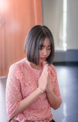 Close-up portrait of a young pretty Asian girl paying respect and praying Buddhism worshiping Buddha statue with faith. Hands begging, put your hands together in a prayer position.