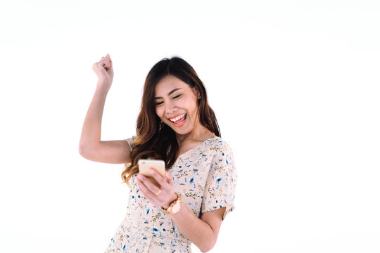 portrait of attractive asian woman smile broadly with happiness while holding phone in hand and raise her arm over head with joy in success on white background, technology and digital concept..