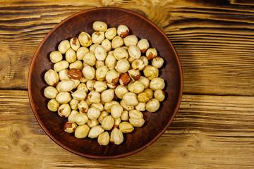 Peeled hazelnuts in ceramic plate on wooden table. Top view