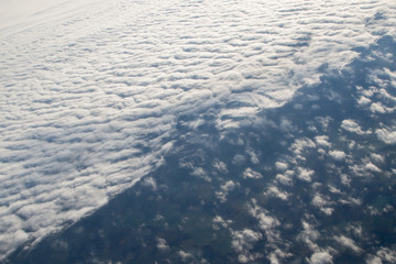 Fluffy cumulus and cirrus clouds separated diagonally in image, the aerial picture is taken from above through the window of the aircraft at an altitude of ten thousand kilometers.
