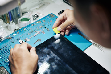 Hands of repairman using guitar pick to remove the screen of digital tablet and check internal...