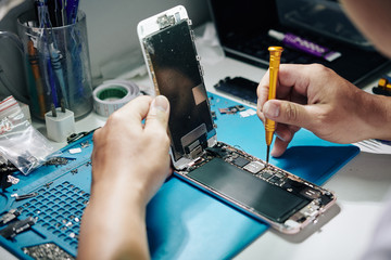 Repairman removing smartphone screen and screws securing SIM card tray