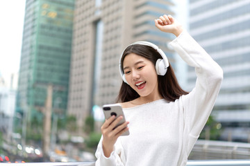 Asian girl wearing headphones listening to music online from smartphone