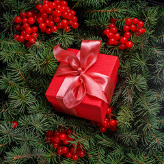 New Year Christmas Xmas 2020 holiday celebration red present gift box with satin pink bow, immersed in the needles of a Christmas tree decorated with red berries. Dark festive composition.