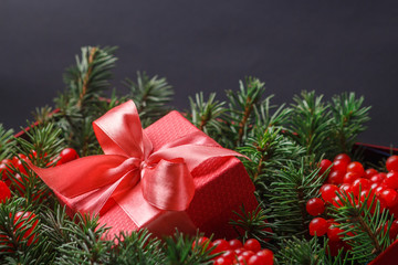 New Year Christmas Xmas 2020 holiday celebration red present gift box with satin pink bow, immersed in the needles of a Christmas tree decorated with red berries. Dark festive composition.