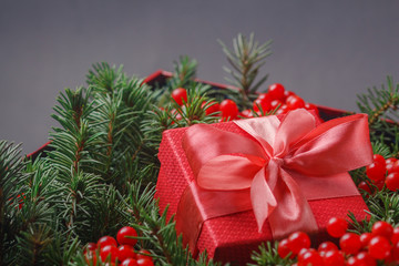 Obraz na płótnie Canvas New Year Christmas Xmas 2020 holiday celebration red present gift box with satin pink bow, immersed in the needles of a Christmas tree decorated with red berries. Dark festive composition.