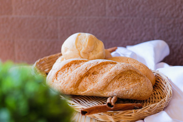 Freshly baked delicious bread on wooden table with white cloth and green plant flowerpot.