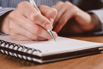 Close up of woman's hands writing in spiral notepad placed on wooden desktop with various items