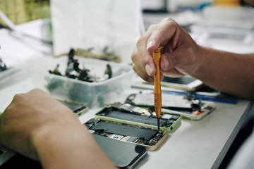 Hands of repairman using pentalob screwdriver when removing smartphone battery