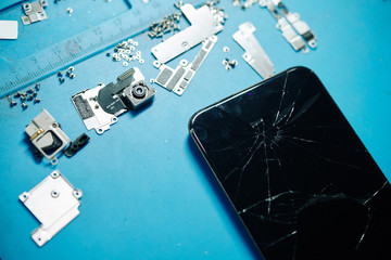 Cracked modern smartphone, broken camera, metal brackets and screws, view from above