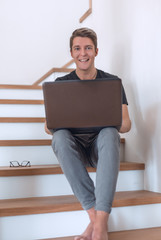 smiling young man in home clothes uses laptop