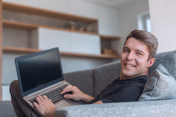 smiling young man with laptop lying on comfortable couch