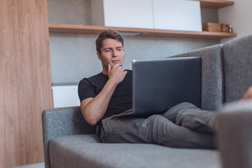 young man using his laptop lying on the sofa in the living room