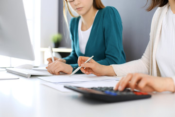 Fototapeta na wymiar Accountant checking financial statement or counting by calculator income for tax form, hands close-up. Business woman sitting and working with colleague at the desk in office. Audit concept