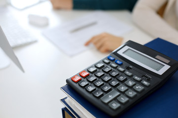 Calculator and binders with papers are waiting to be processed by business woman or bookkeeper working at the desk in office back in blur. Internal Audit and tax concept
