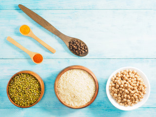 Rice, green gram, allspice, chick pea, allspice, turmeric, chili pepper in cups and spoons on blue wooden background. Indian cuisine, ayurveda, naturopathy, modern apothecary concept