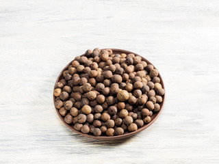 Allspice in clay plate on a white background. Indian cuisine, ayurveda, naturopathy, modern apothecary concept