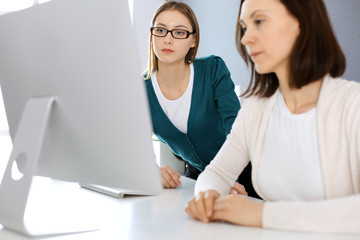 Businesswoman giving presentation to her female colleague while they sitting at the desk with computer. Group of business people working in office. Teamwork concept