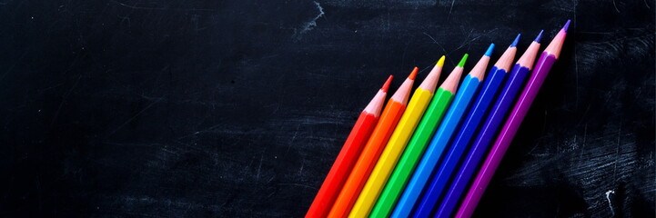 Wide angle panorama or background. Colorful wooden pencils seven colors of rainbow for painting on black chalkboard background with empty copy space for writing your text.