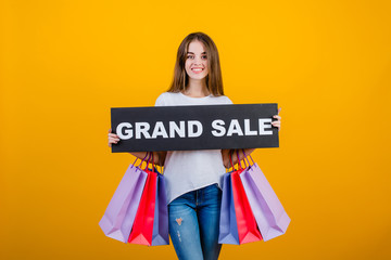 beautiful brunette woman with colorful shopping bags and copyspace text grand sale sign isolated over yellow