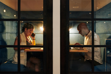 Business lady talking on phone and checking notes when her colleague working on laptop in the room...