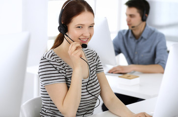 Group of operators at work. Call center. Focus on beautiful woman receptionist in headset at customer service. Business concept and casual striped clothing style