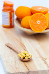 Medicine in wooden spoon on blurred orange slice and bottle capsule background,