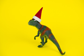 funny green dinosaur toy in little santa claus hat  on vibrant yellow background