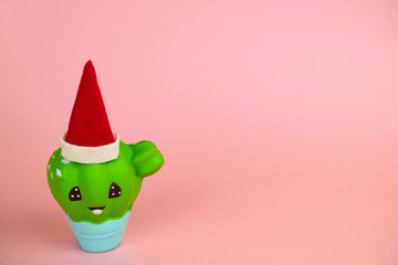 cute christmas and new year card with squishy toy cactus with Santa Claus red hat on a pastel pink background with free space for text