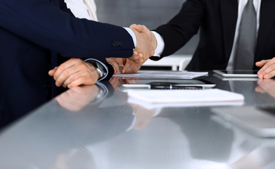 Business people shaking hands after contract signing in modern office. Unknown businessman with colleagues at meeting or negotiation. Teamwork, partnership and handshake concept