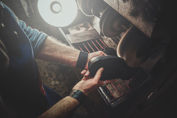 Hands of shoe master, which is working on shoe sole, using special machine tool.