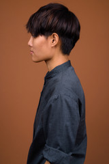 Young beautiful Asian woman with short hair against brown backgr