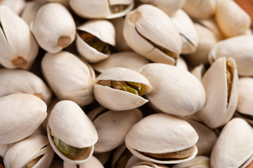  Pistachio in wooden bowl in background with green leaves.