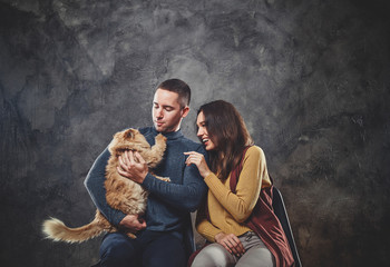 Fototapeta na wymiar Happy attractive couple are sitting at photo studio with fluffy ginger cat.