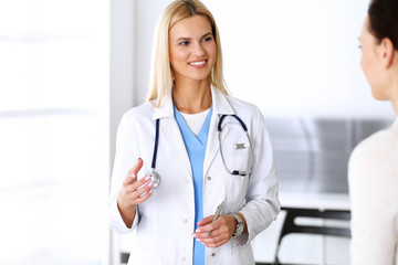 Doctor woman at work in hospital excited and happy of consulting female patient. Blonde physician controls medication history records and exam results while using clipboard. Medicine and healthcare